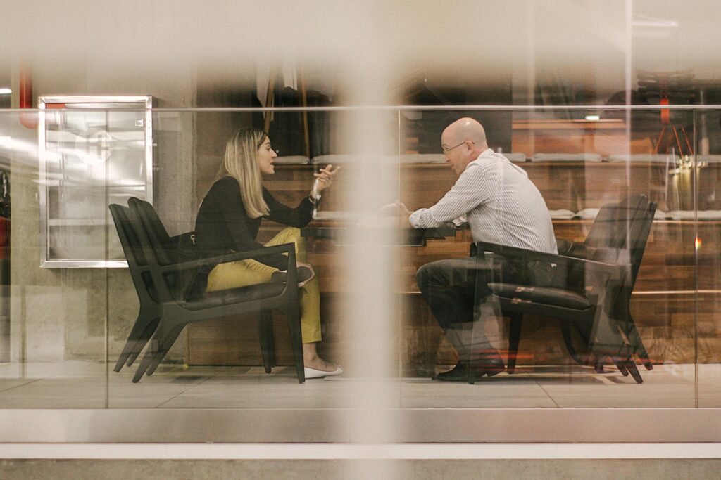 pexels-photo-2379944-2379944 Two professionals engaged in a discussion in a modern office setting through a glass window.
